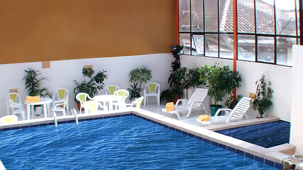 An indoor swimming pool with white lounge chairs and tables, surrounded by potted plants. - Coloso Potosi (Potosi)