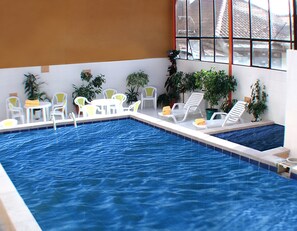 An indoor swimming pool with white lounge chairs and tables, surrounded by potted plants. - Coloso Potosi (Potosi)