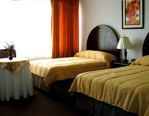 Habitación de hotel con dos camas, una mesa con un jarrón de flores, una lámpara y un cuadro en la pared.