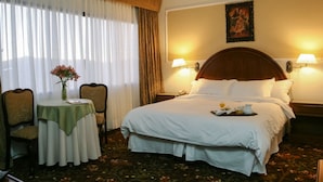 A hotel room with a large bed, two bedside lamps, a nightstand, a table with a vase of flowers, and a chair. - Coloso Potosi (Potosi)
