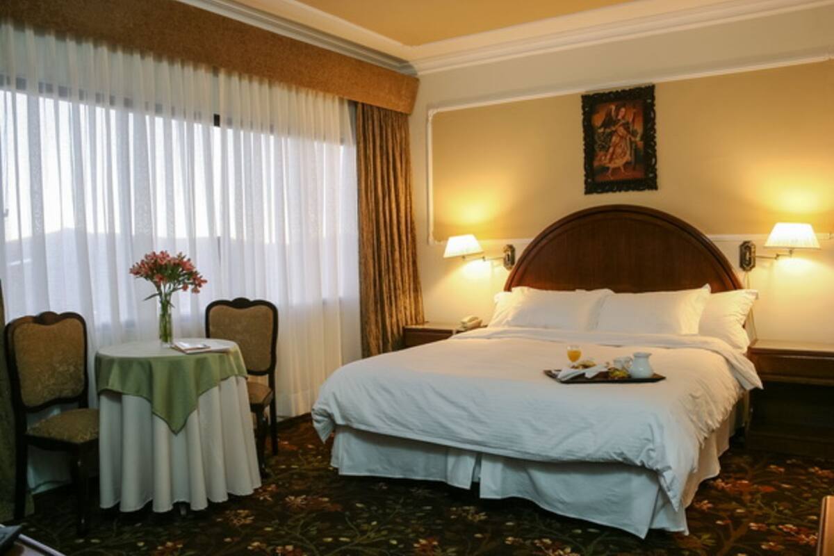 Una habitación de hotel con una cama grande, dos lámparas de noche, una mesita de noche, una mesa con un jarrón de flores y una silla.