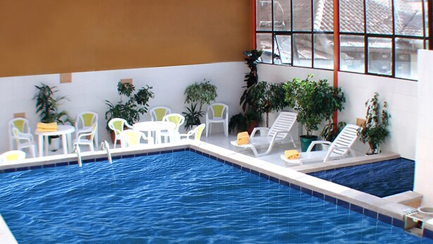 An indoor swimming pool with white lounge chairs and tables, surrounded by potted plants. - Coloso Potosi (Potosi)