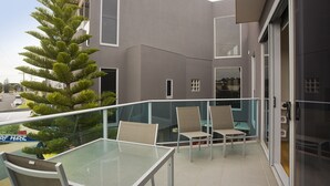 A balcony with a glass table and chairs, a potted plant, and a view of a modern building. - 7 Bell Street Apartments (Torquay)