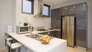 A modern kitchen with stainless steel appliances, a white countertop, and a fruit bowl. - 7 Bell Street Apartments (Torquay)