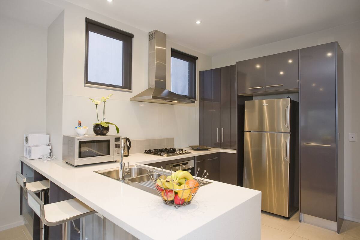 A modern kitchen with stainless steel appliances, a white countertop, and a fruit bowl.