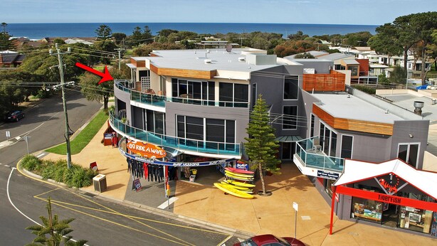 A modern building with a glass balcony, a surf shop, and a view of the ocean. - 7 Bell Street Apartments (Torquay)