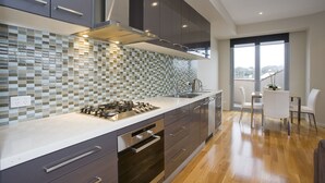 A modern kitchen with grey cabinets, a stainless steel stove, and a tiled backsplash. - 7 Bell Street Apartments (Torquay)