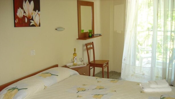 Habitación de hotel con cama, una silla, mesita de noche, espejo y ventana con cortinas.
