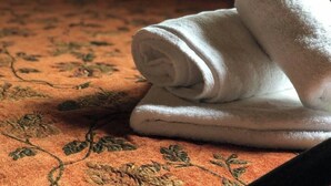 Una toalla blanca doblada con cuidado sobre una cama con una colcha estampada de flores.