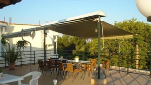 Un patio al aire libre con mesas y sillas, una zona de estar cubierta y macetas con plantas.