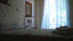 Un dormitorio con una cama, una silla, una mesita con una botella y vasos, y una ventana con cortinas.