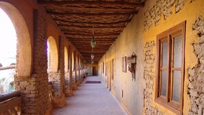 A corridor with stone walls, wooden beams, and arched windows. - Kasbah Hotel Xaluca Arfoud (Aarab Sebbah Ziz)