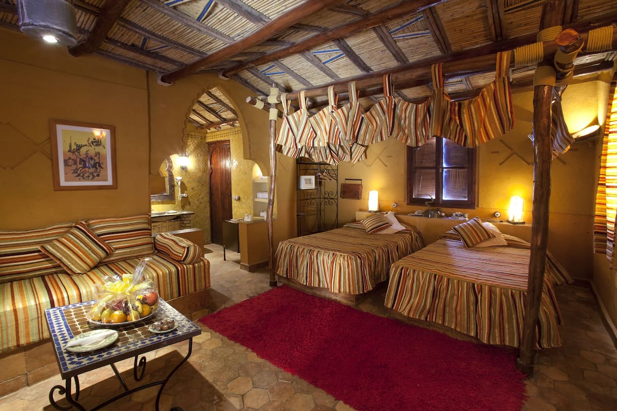 A cozy room with two beds, a sofa, and a dining table with fruit.