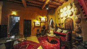 A traditional interior with a wooden ceiling, a red carpet, a dining area with a table and chairs, and a seating area with a sofa and cushions. - Kasbah Hotel Xaluca Arfoud (Aarab Sebbah Ziz)