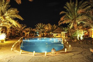 A nighttime swimming pool surrounded by palm trees and outdoor seating areas. - Kasbah Hotel Xaluca Arfoud (Aarab Sebbah Ziz)