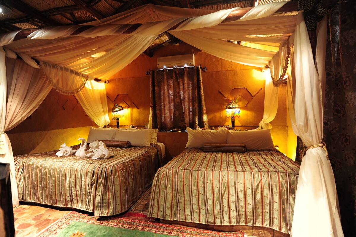 A room with two beds, each with a canopy and pillows, a mirror, and a wall-mounted air conditioner.