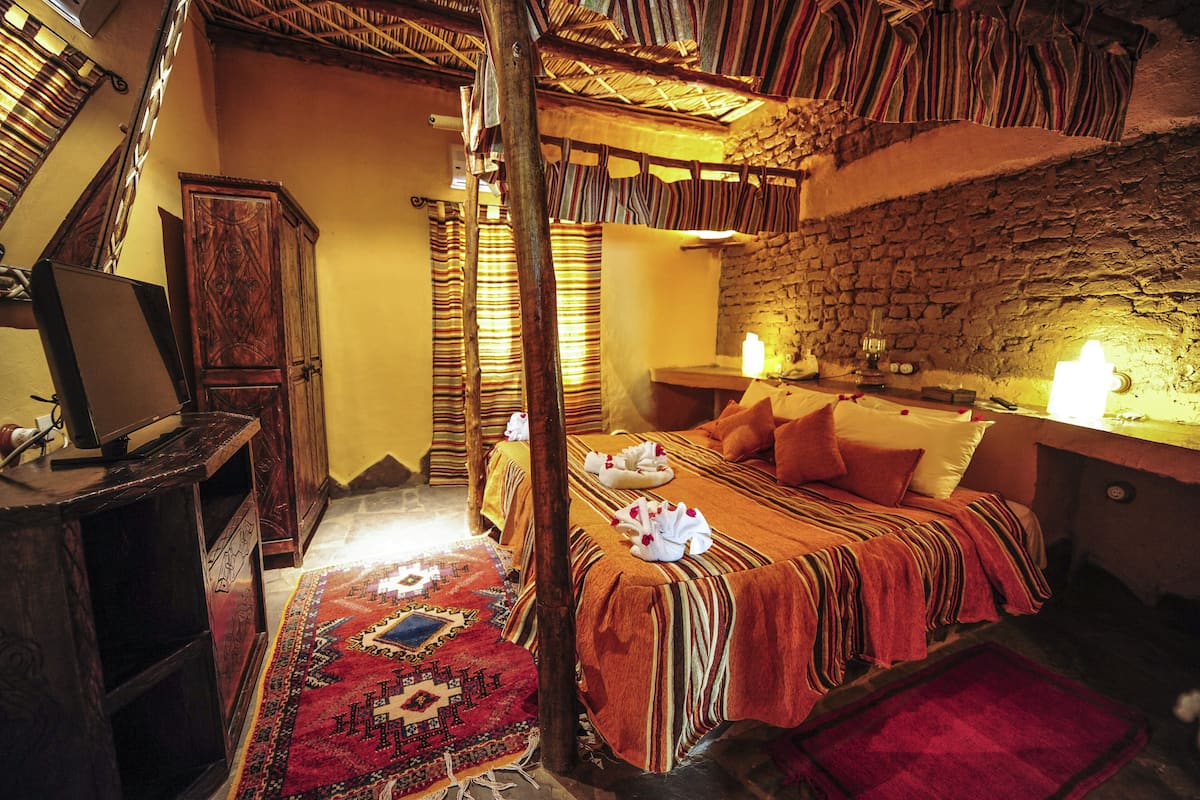 A traditional room with a bed, a wooden wardrobe, a desk with a laptop, and a stone wall.
