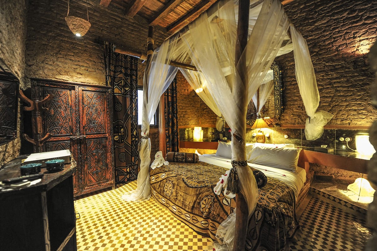 A traditional room with a canopy bed, checkered floor, and ornate wooden doors.