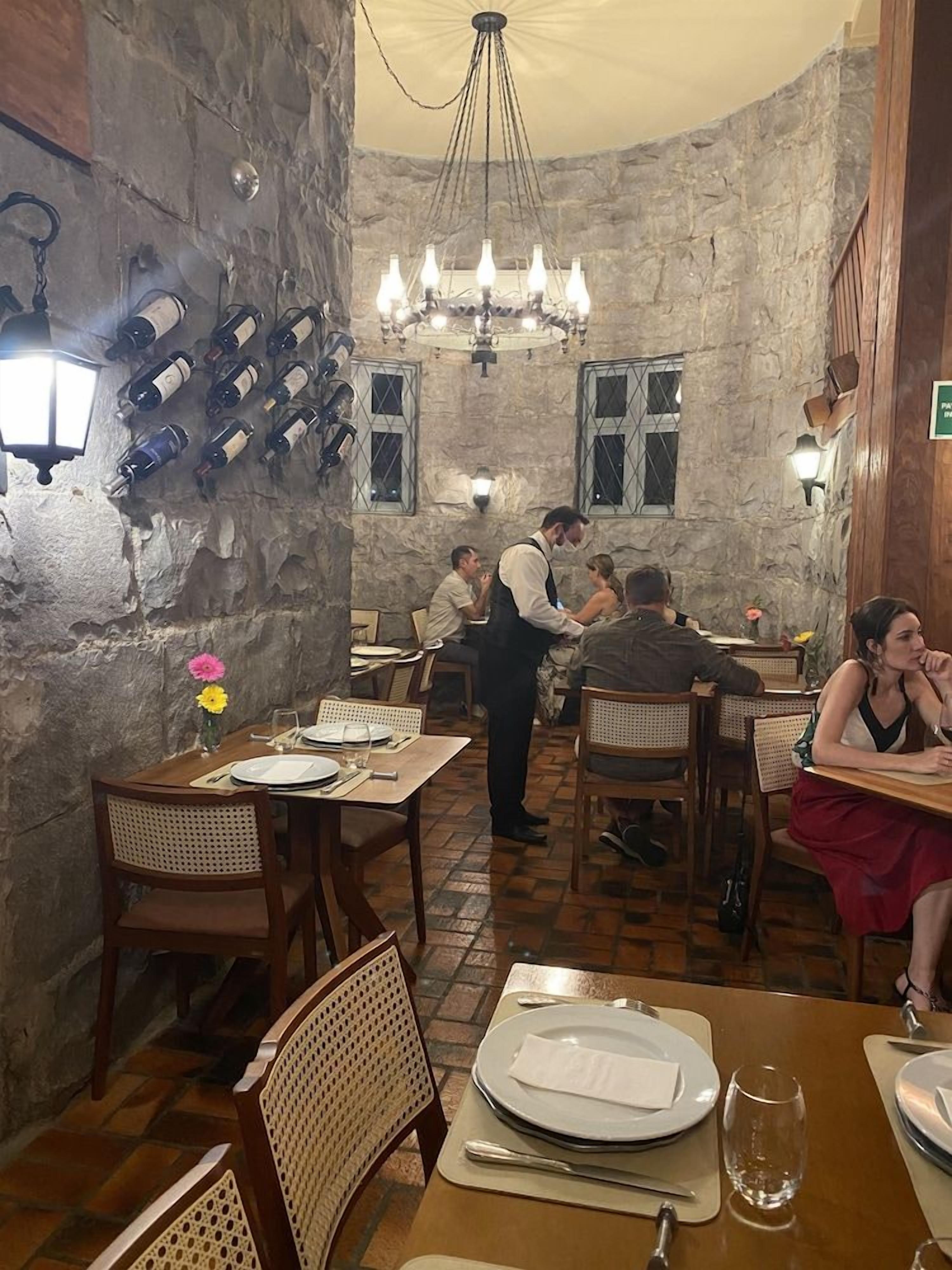 Restaurante com paredes de pedra, mesas de madeira e um lustre.