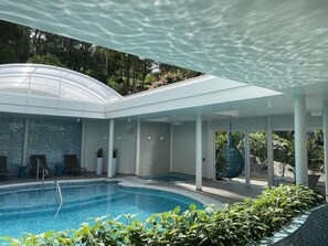 An indoor swimming pool with a glass ceiling, lounge chairs, and a view of the surrounding greenery. - Hotel Casacurta (Garibaldi)