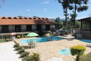 A pool area with stone flooring, umbrellas, and lounge chairs. - Pousada Recanto do Teimoso - Pouso Alegre (Pouso Alegre)