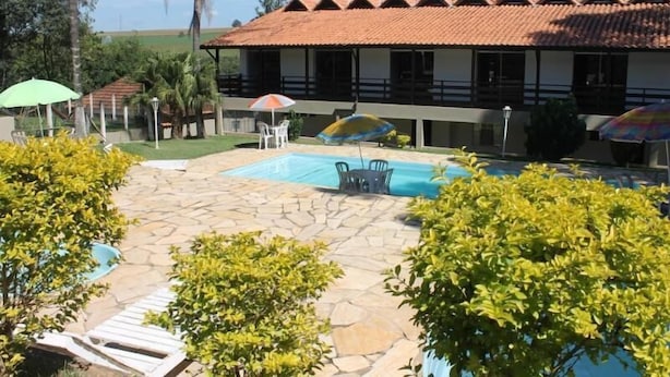 A pool area with lounge chairs, umbrellas, and a building with a tiled roof.