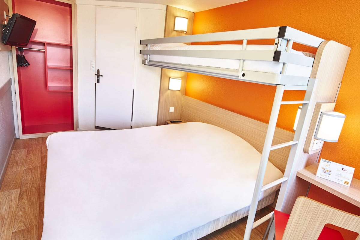 A bunk bed room with a red door, a small bedside table, and a wall-mounted lamp.