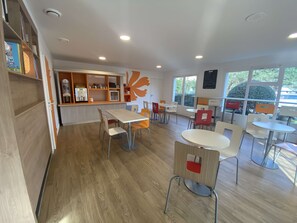 A modern dining area with wooden flooring, multiple tables and chairs, and a service counter with a coffee machine. - Première Classe Nantes Sud - Rezé Aéroport (Reze)