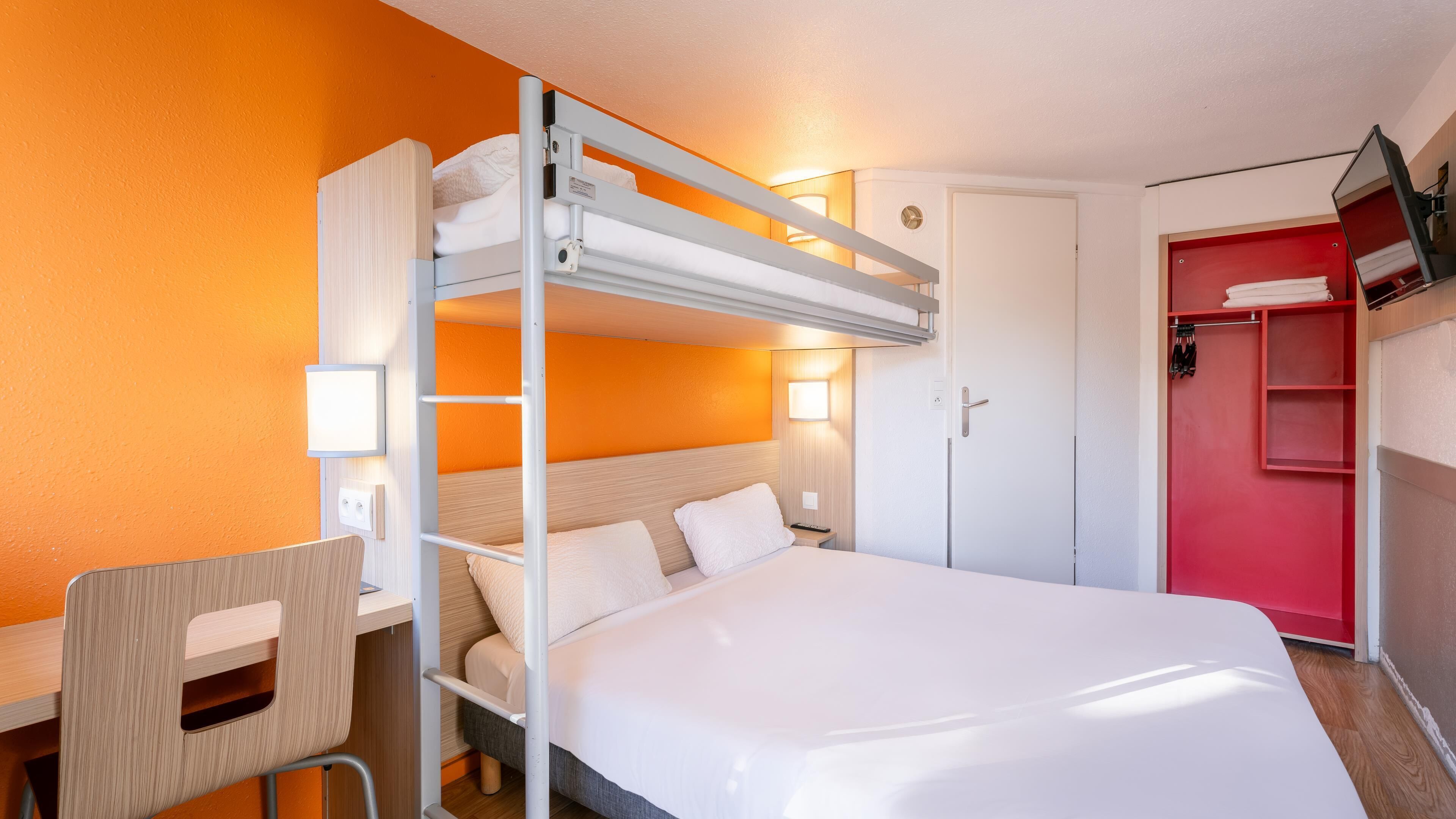 Una habitación de hotel con literas, un escritorio, una silla, un armario y un espejo.