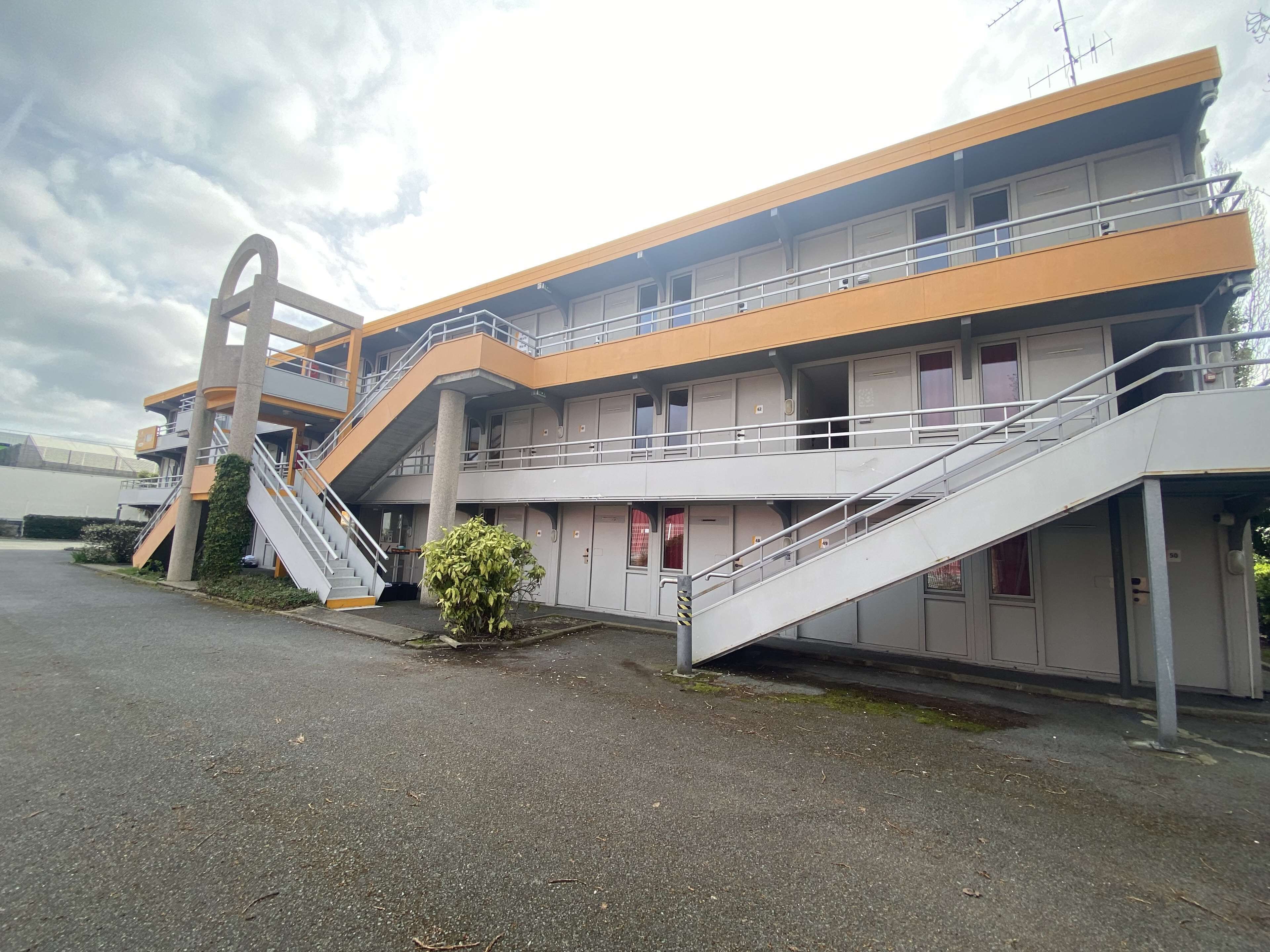Un immeuble à plusieurs étages doté d’un escalier central, de nombreux balcons et d’un espace de stationnement.