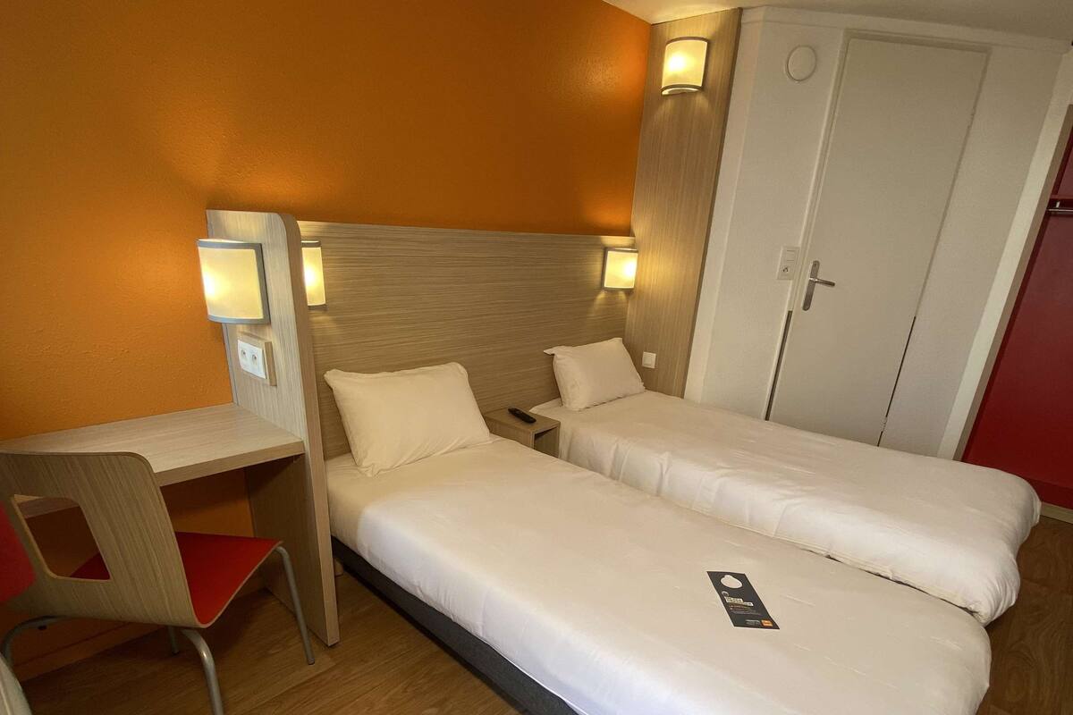 A hotel room with two single beds, a desk with a chair, and a wardrobe.