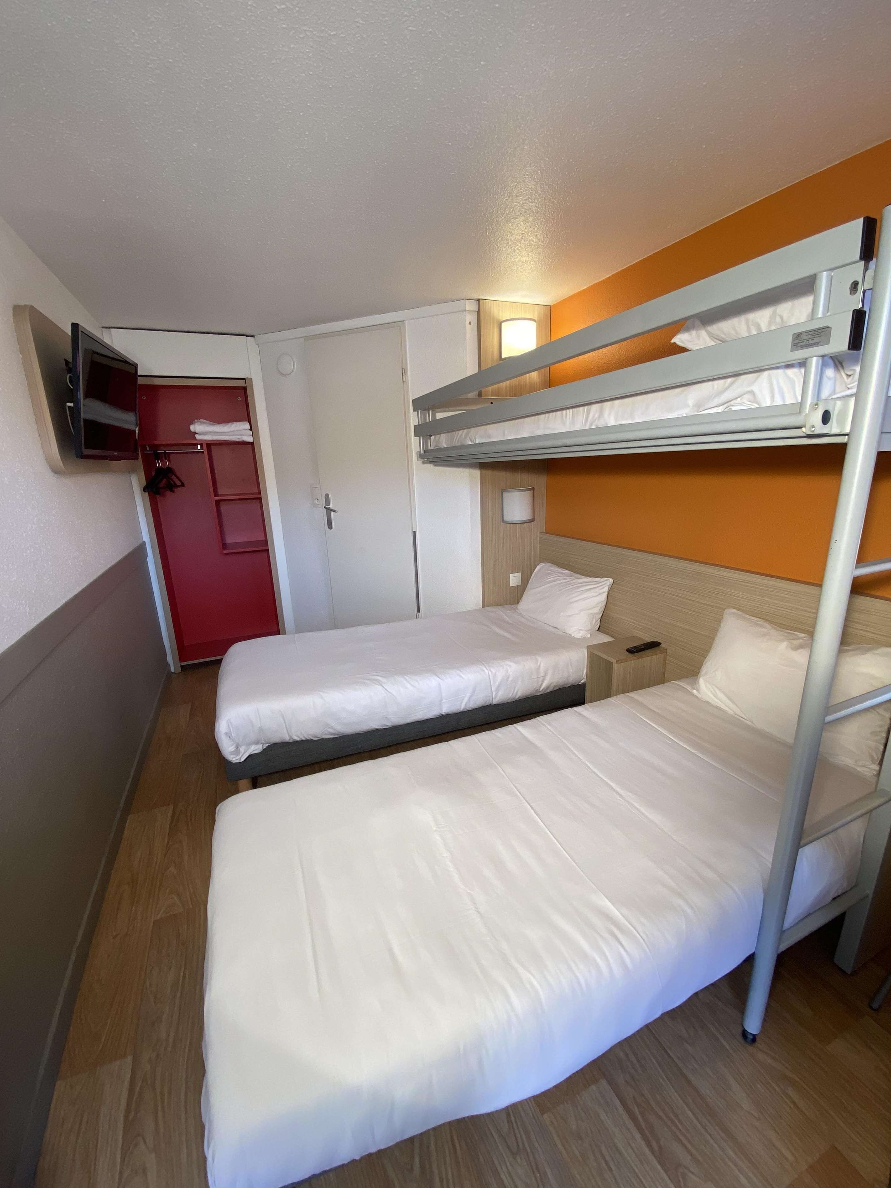 A compact hotel room with two single beds, a red wardrobe, a television mounted on the wall, and a wooden floor.