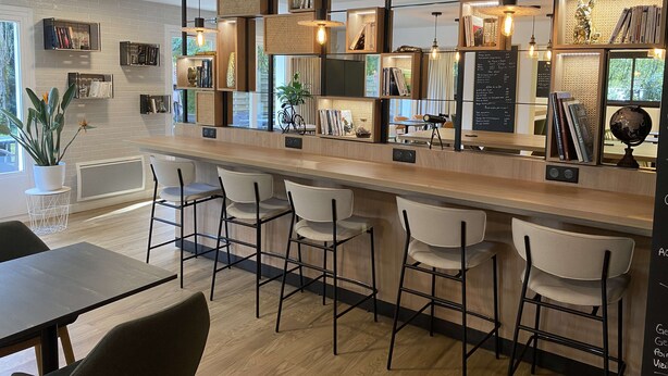 A modern bar area with a wooden counter, white chairs, and shelves with books and decorative items.