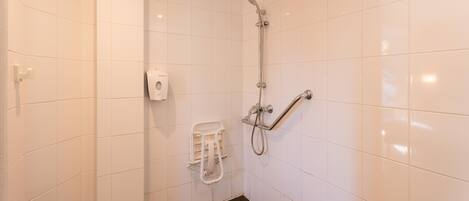 Un baño pequeño con azulejos blancos, ducha, dispensador de jabón y barra de toallas.