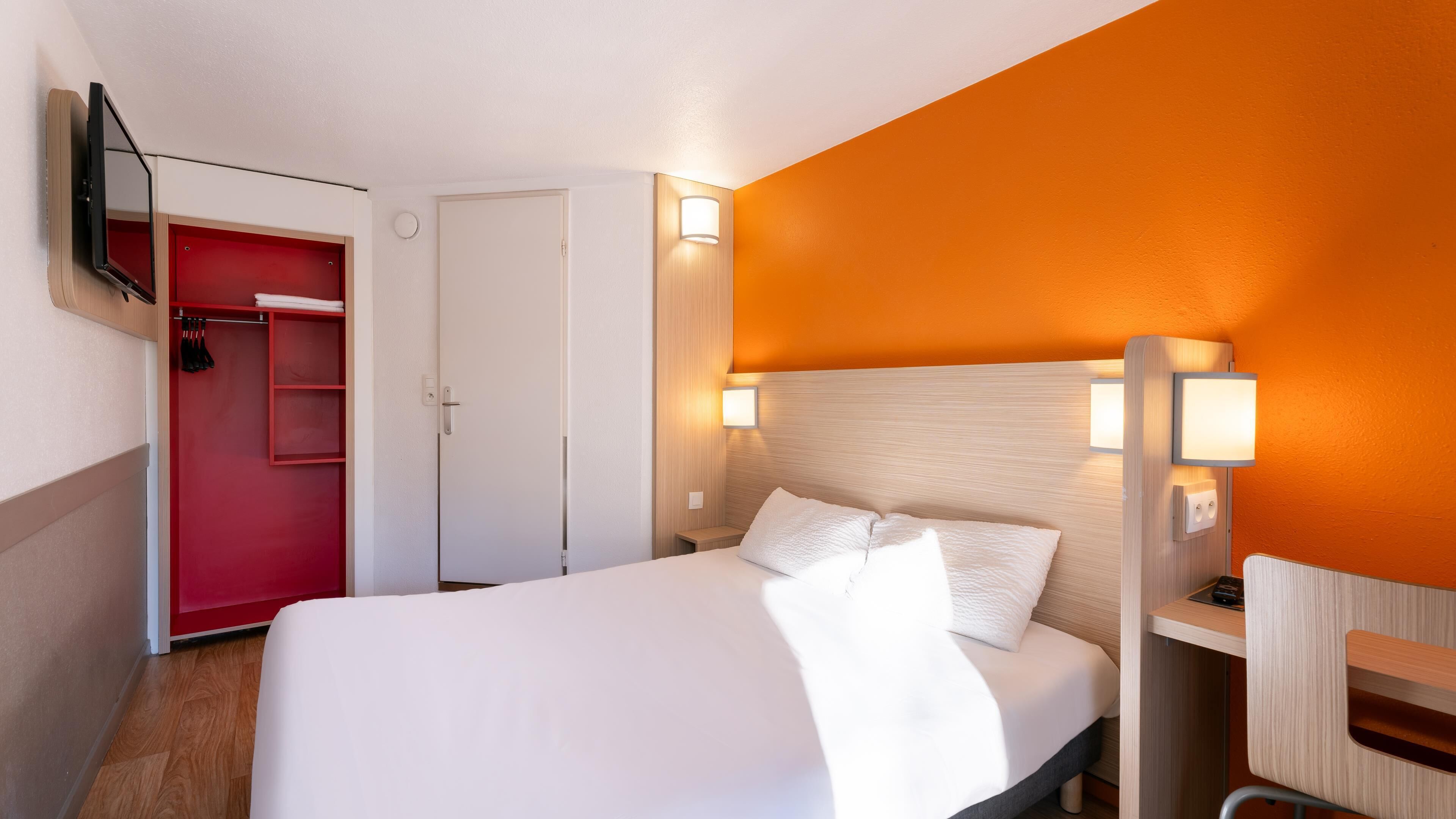 Une chambre d’hôtel avec un lit, un bureau, une télévision, une armoire et une porte.