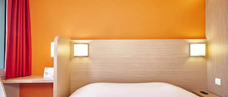 Une chambre d’hôtel équipée d’un lit, d’un bureau, d’une chaise et de deux lampes fixées au mur.