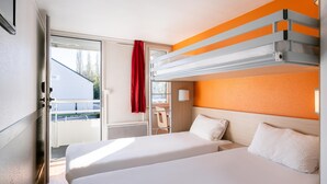 A hotel room with a bunk bed, a sliding door to the outside, a red curtain, and a view of a building and trees.