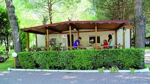 Un espace extérieur abrité, avec une table et des chaises, entouré d’une haie et d’arbres.