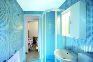 A bathroom with blue mosaic tiles, a white sink, and a mirror above it. - Village Camping Joker (Cavallino-Treporti)