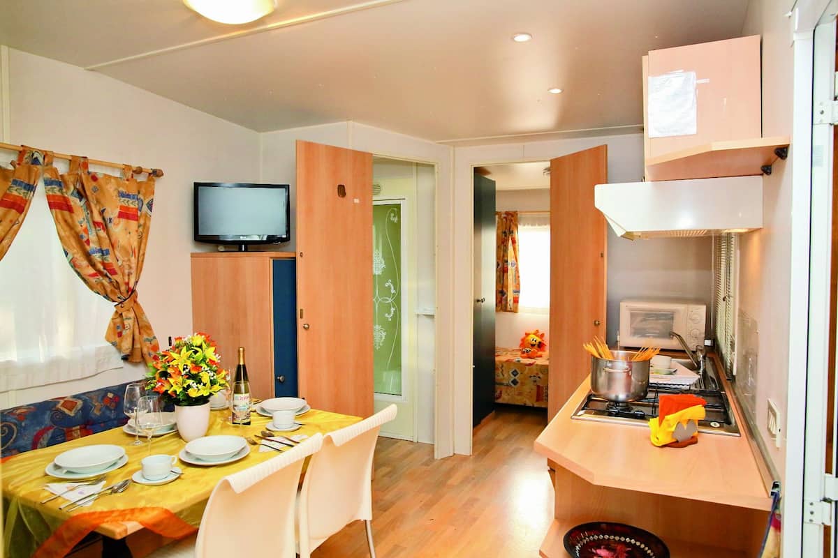 Une chambre d’hôtel compacte comprenant un coin repas, une kitchenette, un téléviseur et un petit lit.