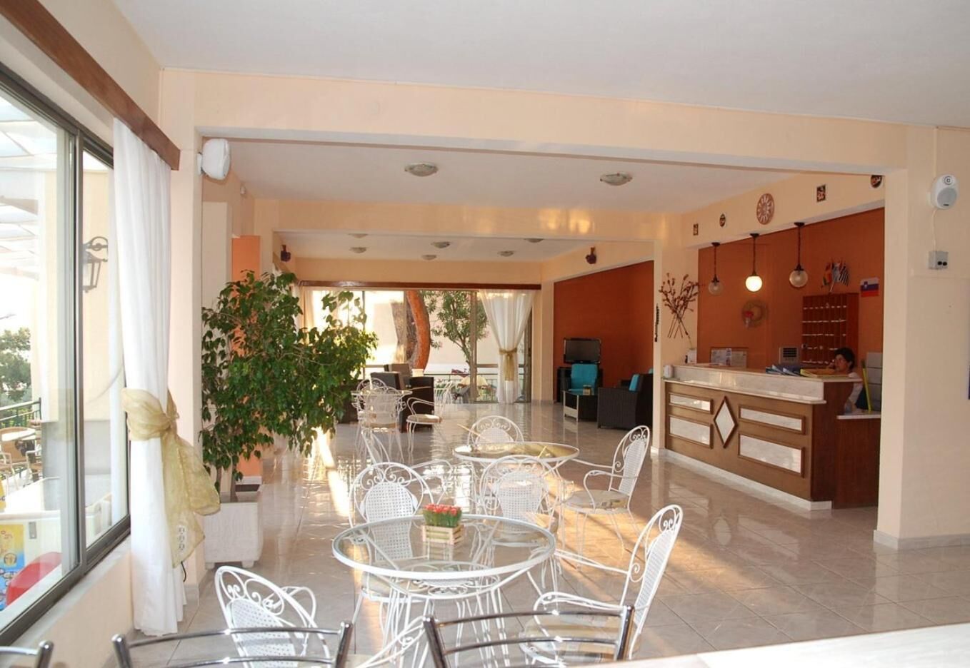 A hotel lobby with a reception desk, seating area with round tables, and a large window with curtains.