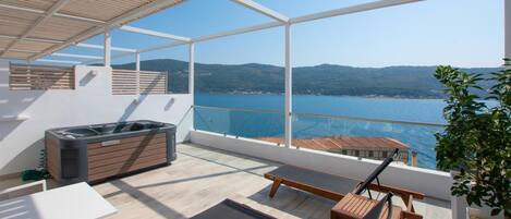 Un balcón con vista al mar, muebles de madera y un jacuzzi.