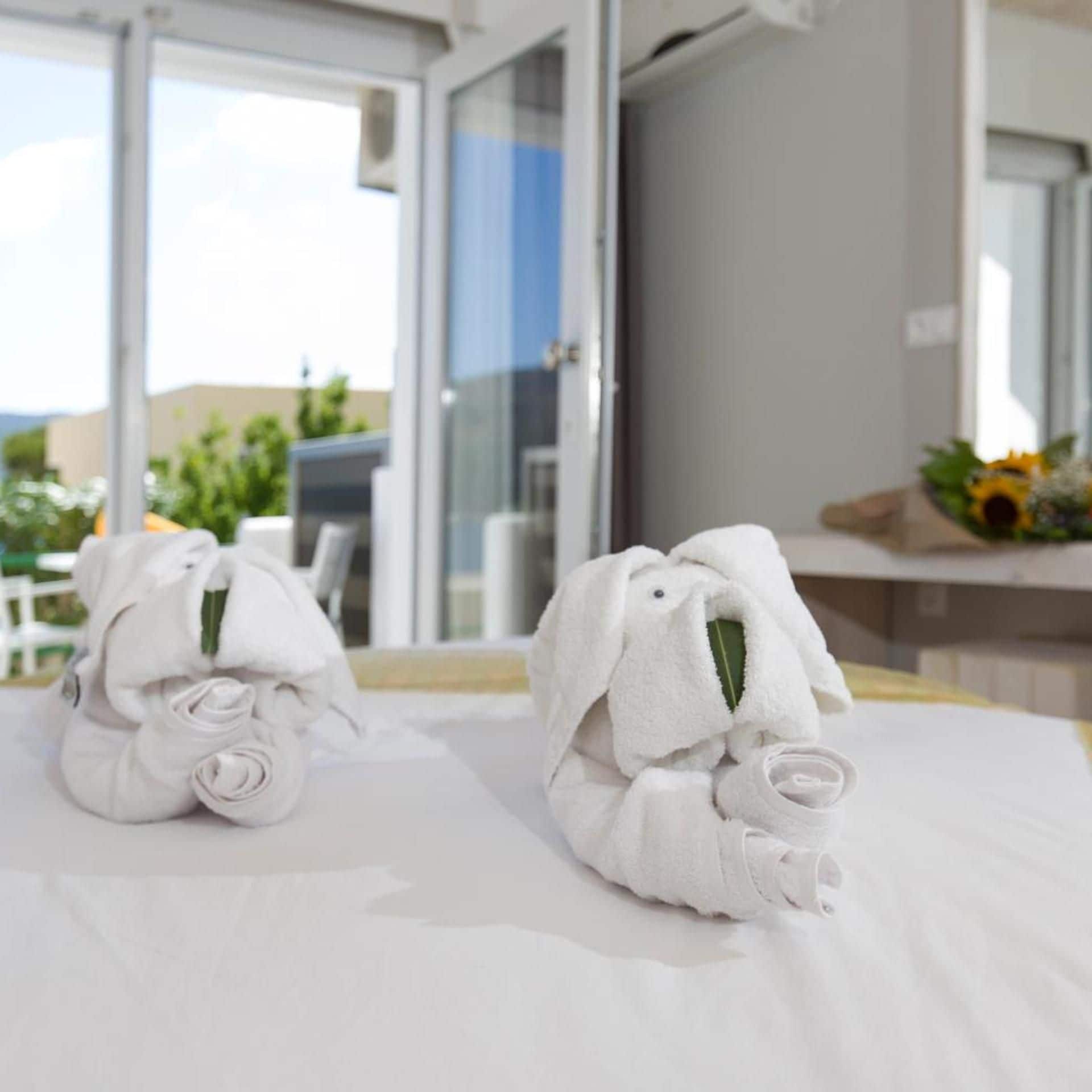 Two towels folded into animal shapes on a bed with a view of a balcony.