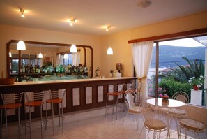 Zona de bar con un espejo grande, taburetes y vista al mar a través de una ventana.