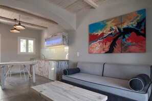 A modern kitchen with a dining area, a gray sofa, and a colorful abstract painting.