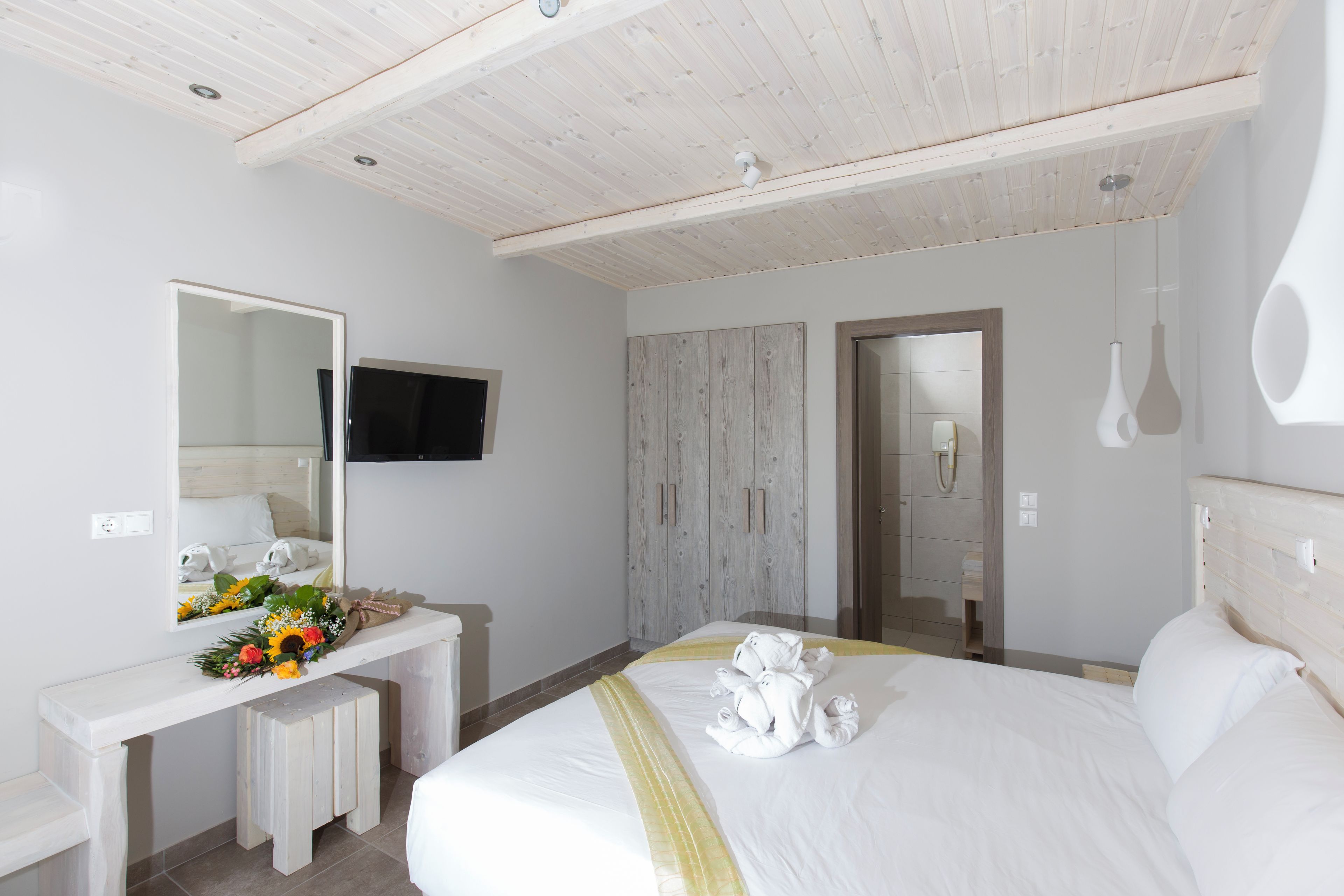 Una habitación de hotel con una cama grande, un tocador con espejo, una televisión y un armario.