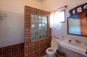 Une salle de bain avec un mur carrelé, une fenêtre à verre dépoli, des toilettes, un lavabo et un miroir.