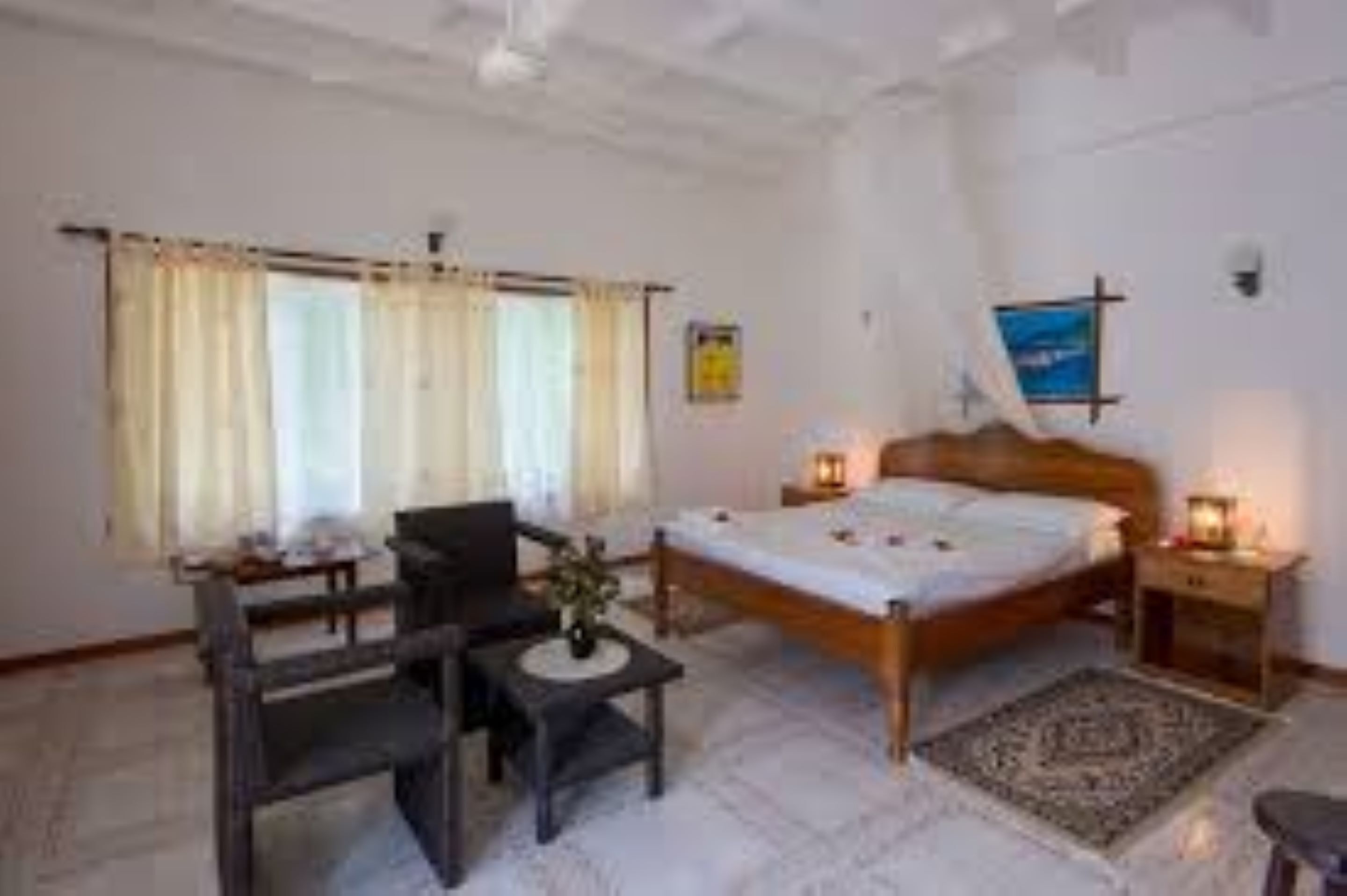 Un dormitorio con cama, mesita de noche, lámpara, silla y ventana con cortinas.