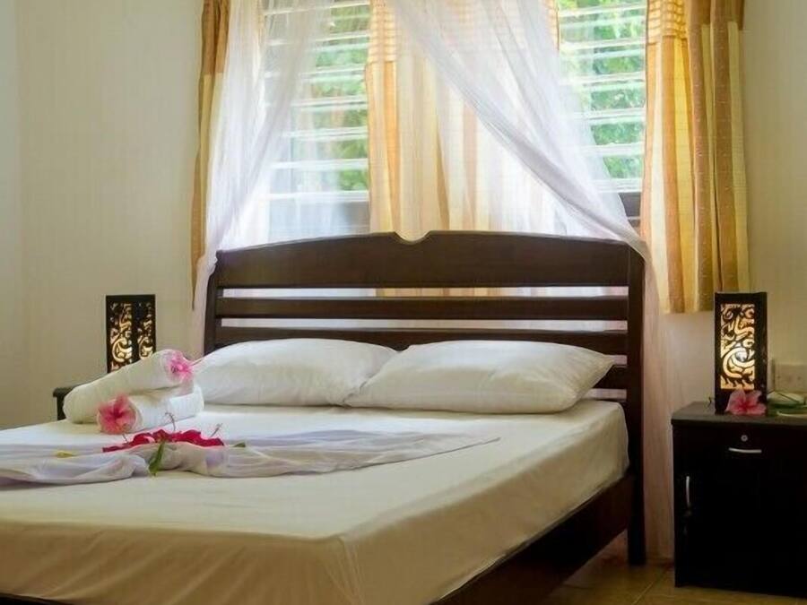 Una cama bien hecha con dosel, una mesita de noche con lámpara y una alfombra roja en el suelo.