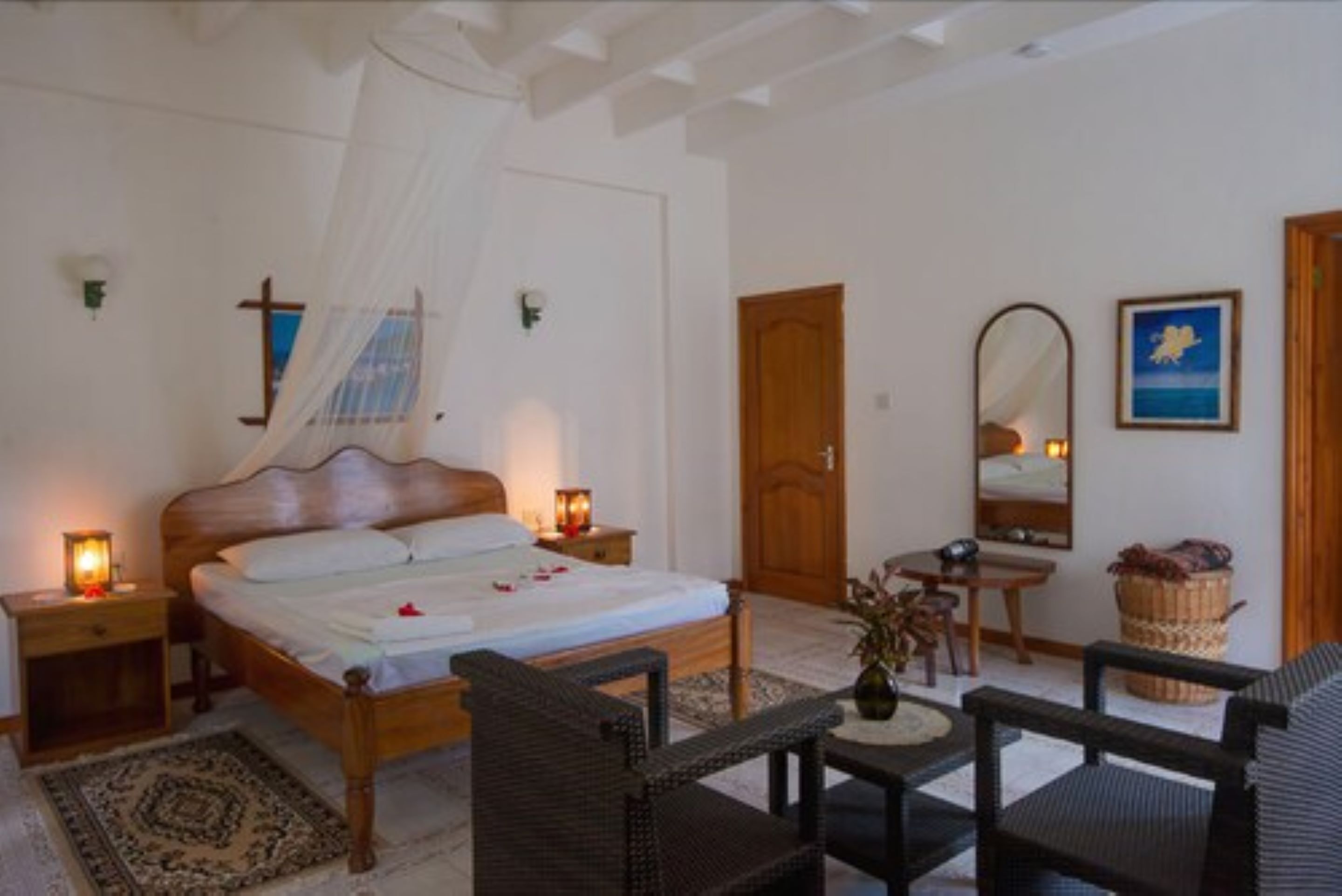 A bedroom with a wooden bed, bedside tables with lamps, a small table with chairs, a mirror, and a framed picture on the wall.